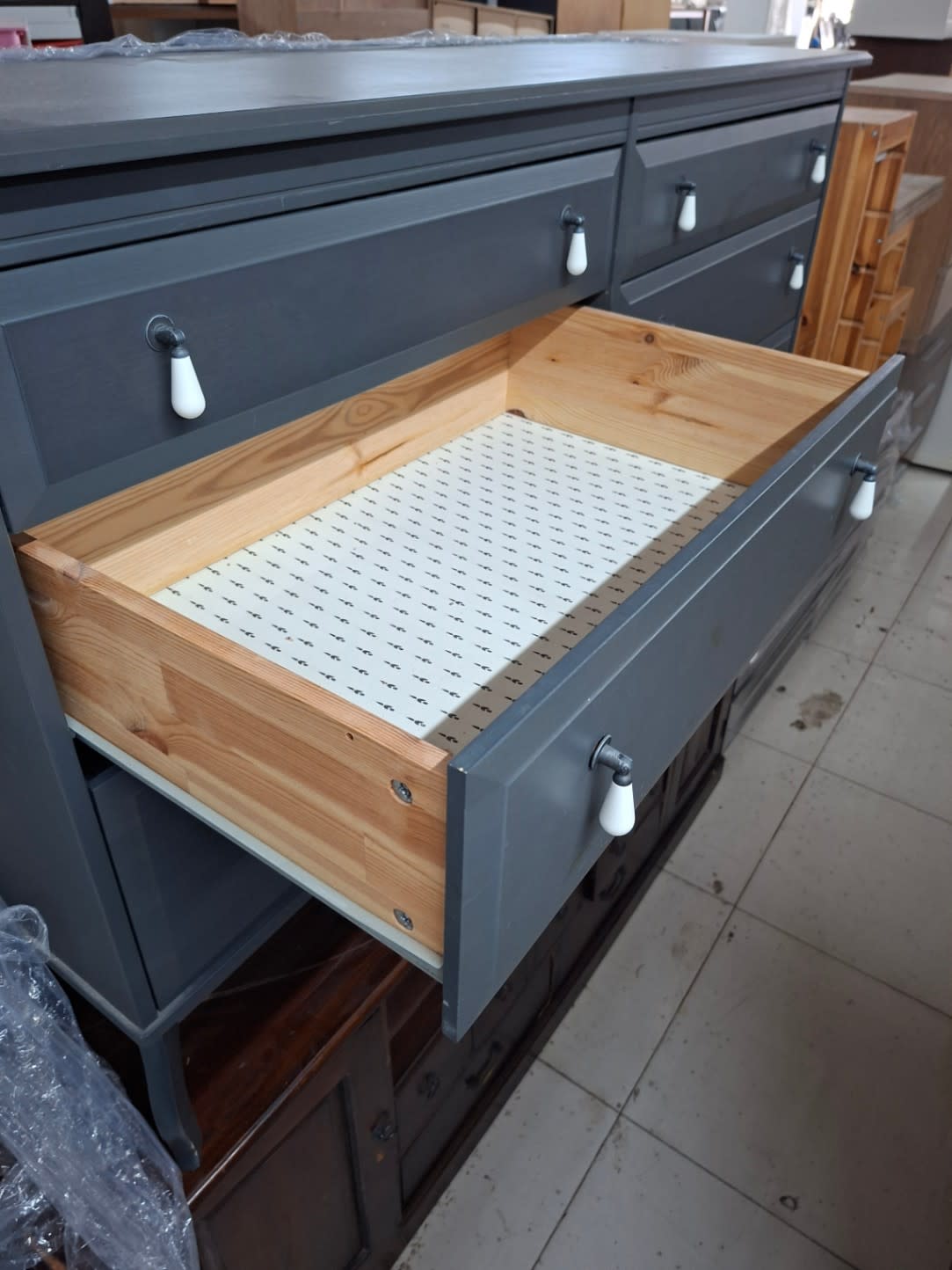 Open bottom drawer of used grey 6-drawer dresser showing pine wood construction and patterned liner