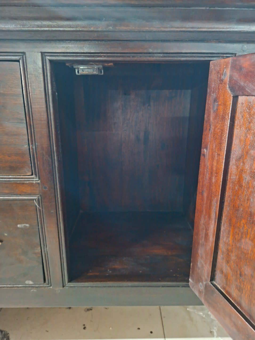 Interior cabinet compartment of used dark wood sideboard with door open showing storage space
