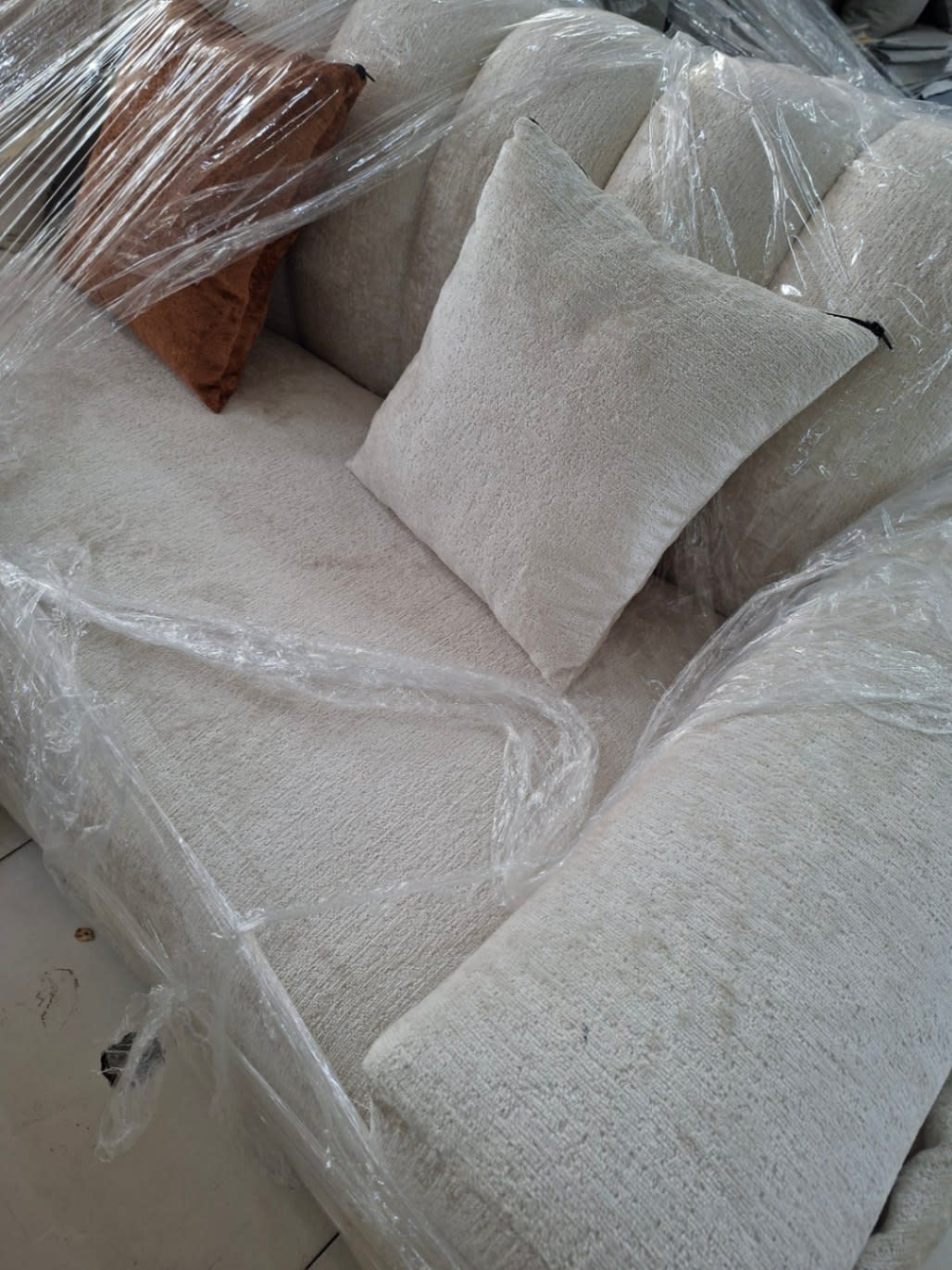 Corner seat detail of new cream L-shape sectional sofa wrapped in protective plastic at Bufaisal Ajman