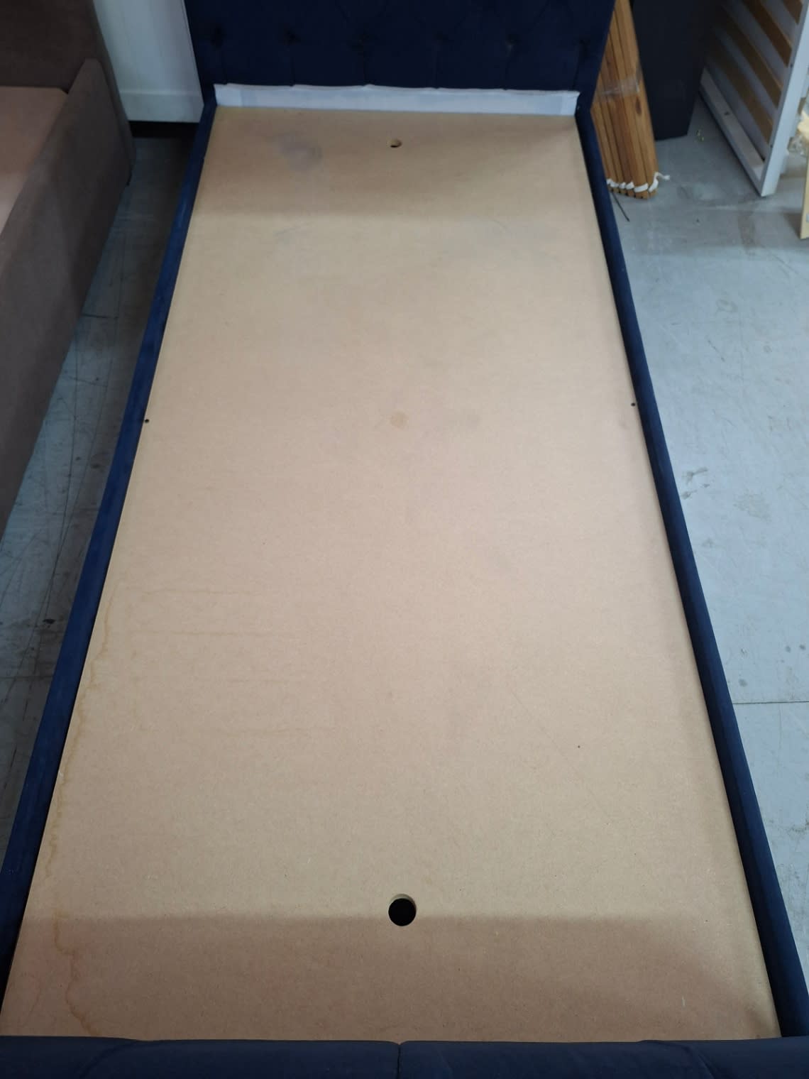 Top-down view of MDF base panel on used single navy blue tufted bed frame showing surface marks