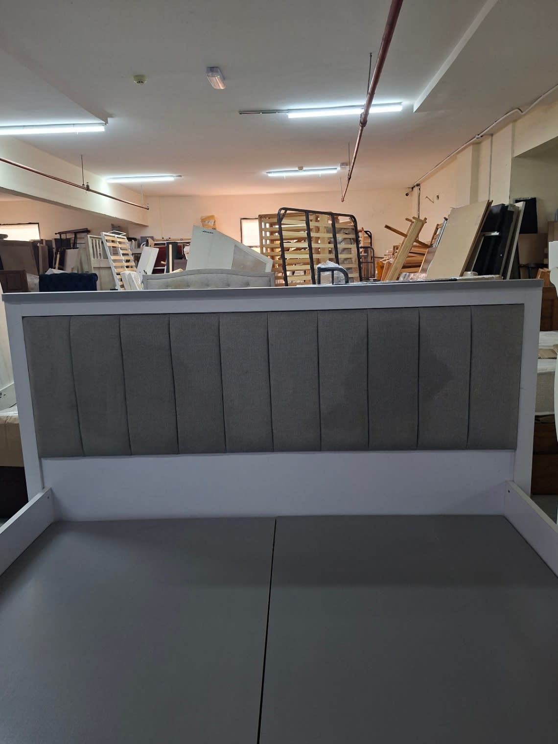 Front view of grey vertical channel-tufted upholstered headboard on white king bed frame at Bufaisal