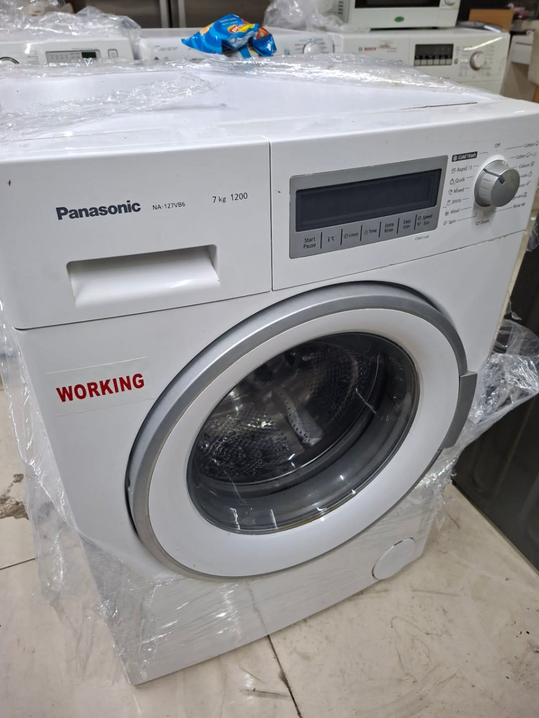 Side angle view of used Panasonic NA-127VB6 7kg front-load washing machine showing overall condition at Shop C Ajman