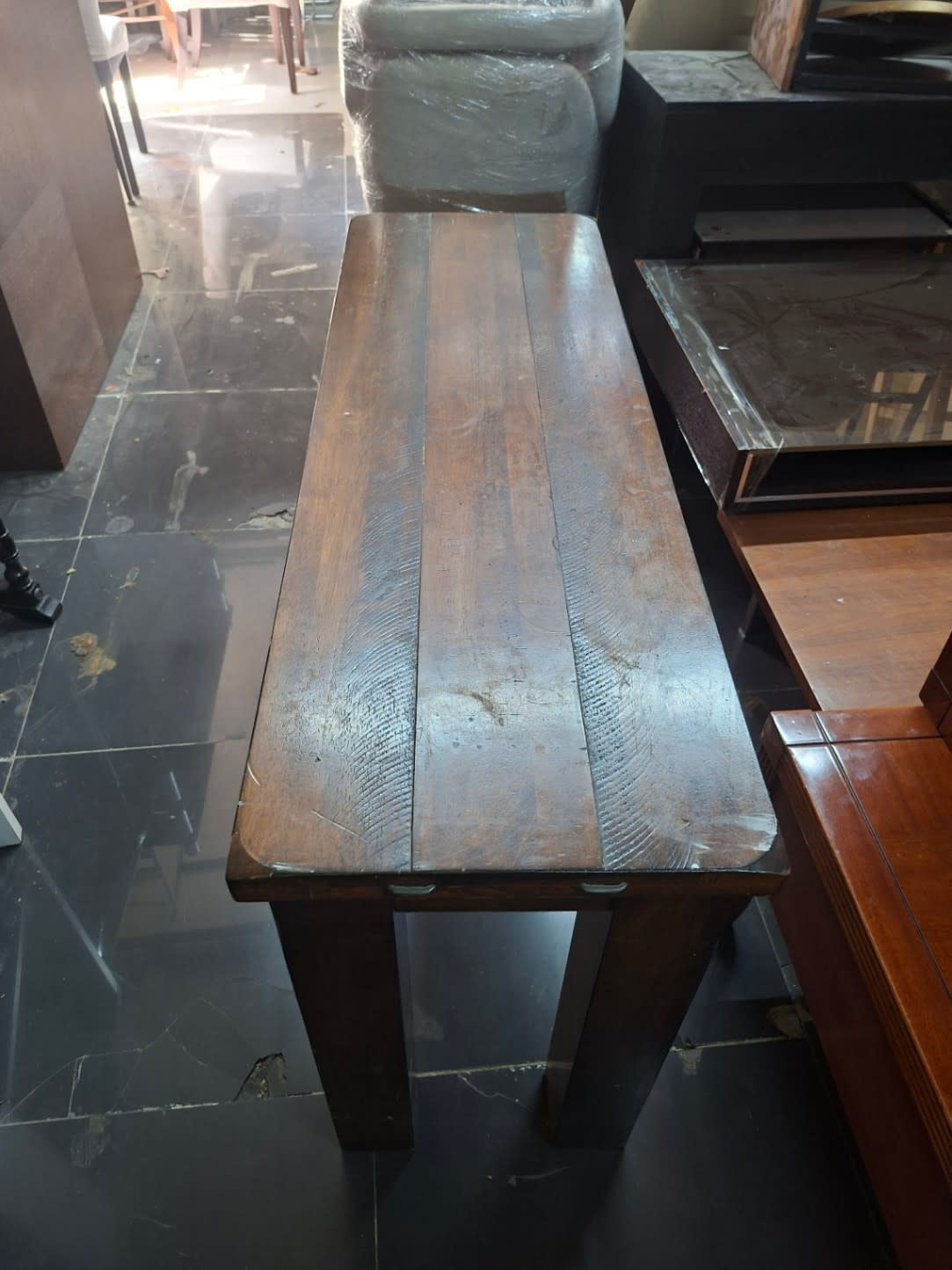 End view of used dark brown solid wood console table showing plank top and four legs