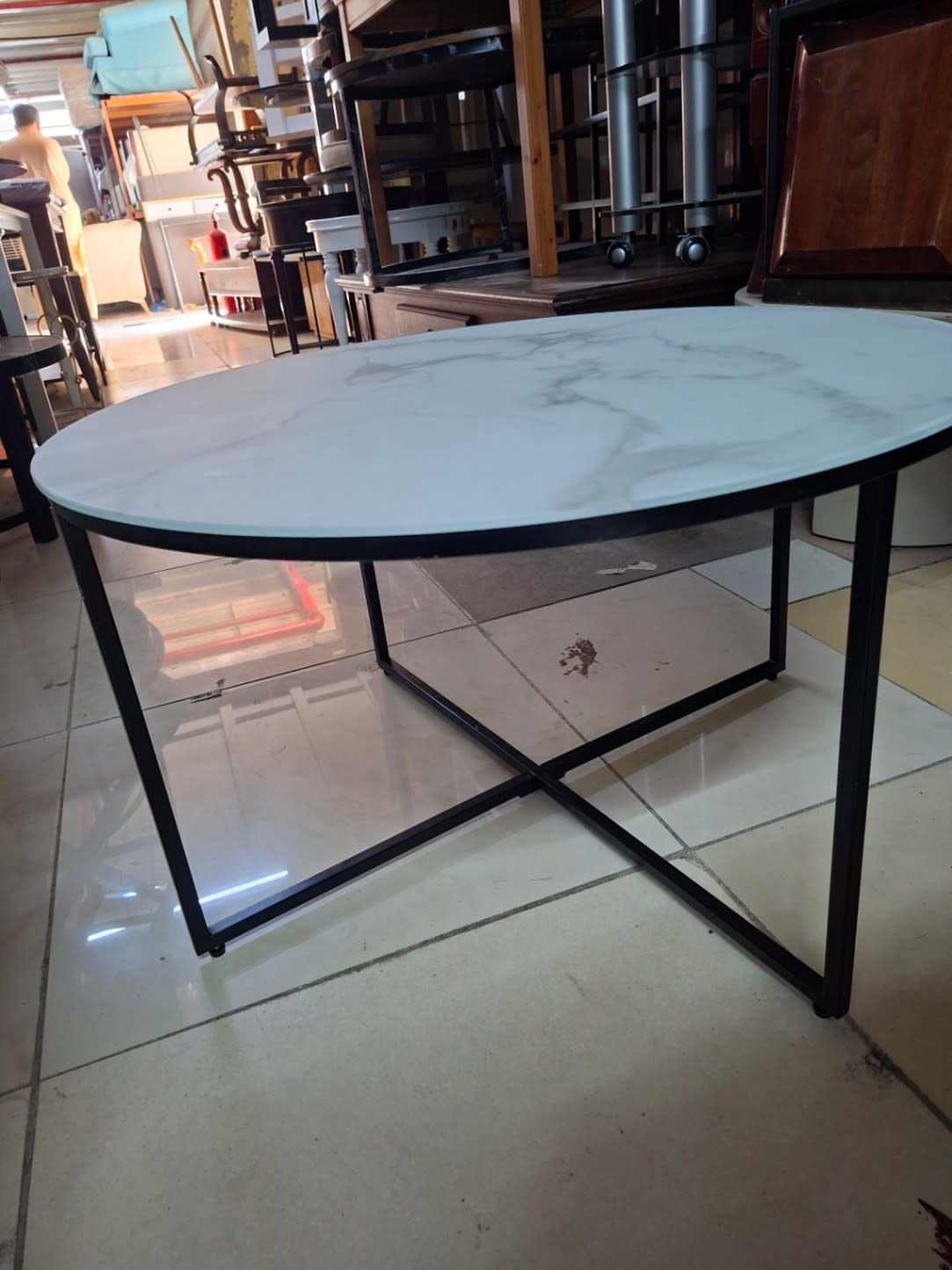 Side angle view of used round coffee table showing black cross-frame base and marble-effect top