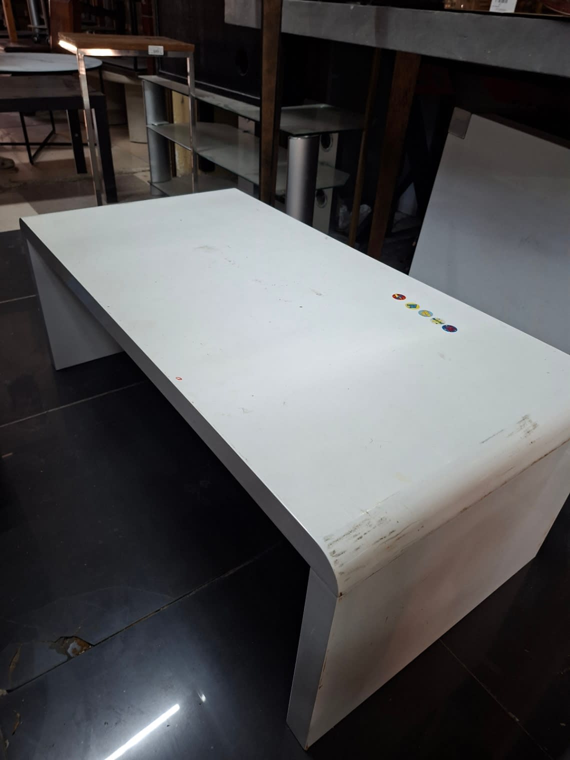 Side angle of used white high-gloss waterfall coffee table showing lower panel scuffs