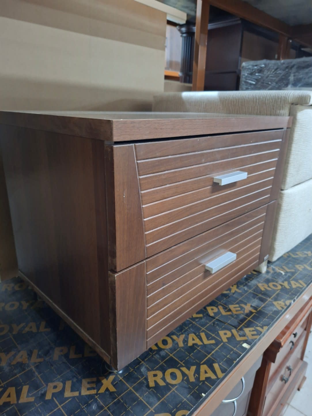 Side angle of used walnut brown 2-drawer bedside table showing edge and chrome feet