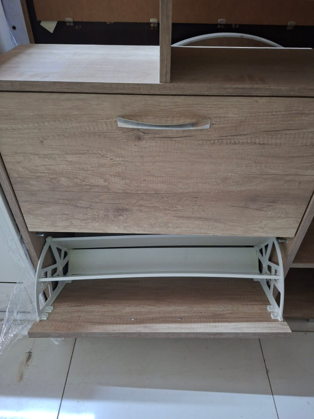 Bottom flip-door compartment open on used oak shoe cabinet showing internal storage tray