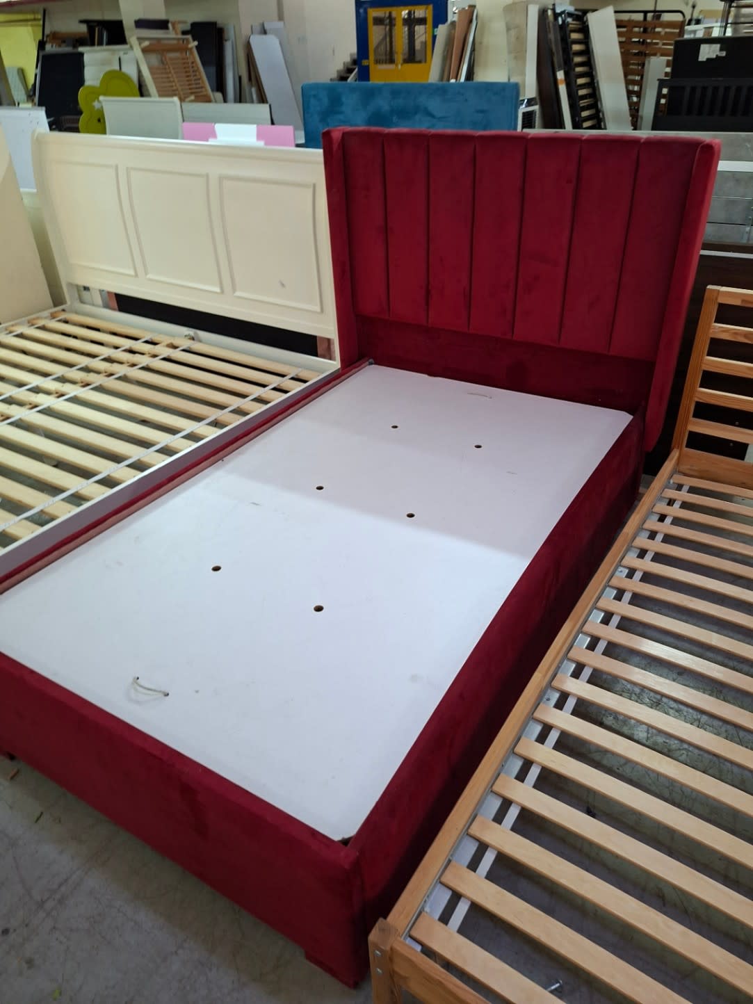 Side angle of used red velvet upholstered bed frame with under-mattress storage base at Bufaisal Ajman