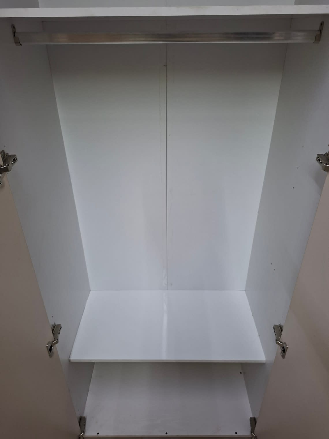 Close-up interior of new white wardrobe showing hanging rail and lower shelves at Bufaisal Ajman