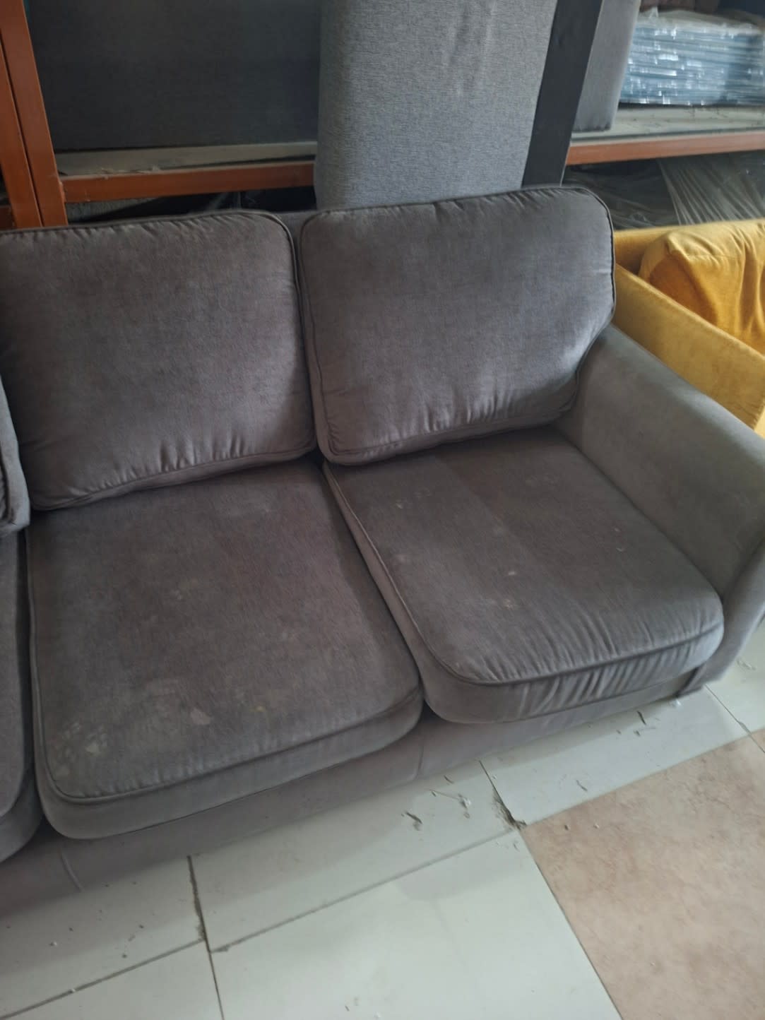 Close-up of seat cushions on used grey fabric sofa showing compression and light staining