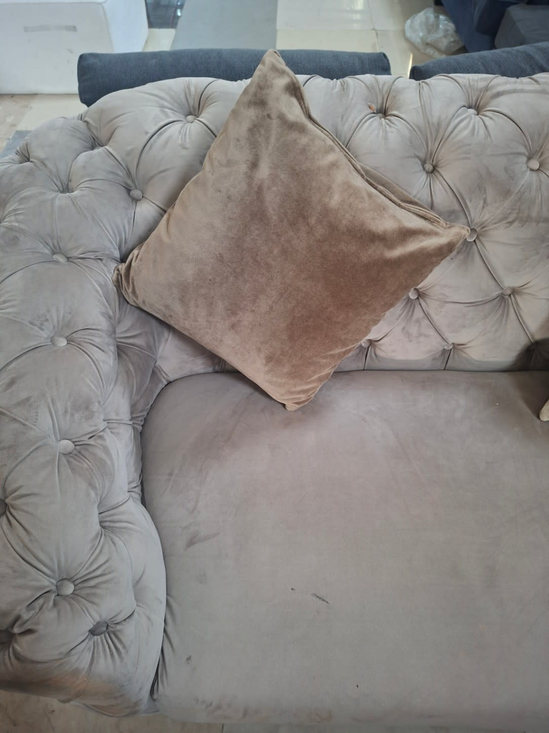 Close-up of seat surface on used taupe Chesterfield sofa showing visible scuff marks and tufting detail