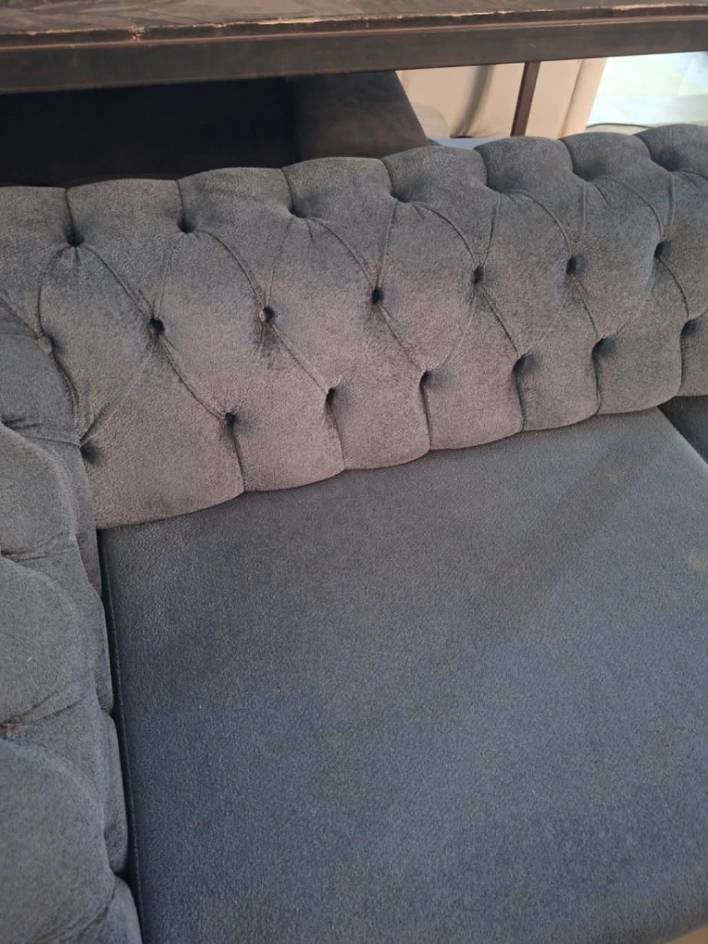 Close-up of tufted back fabric on used grey Chesterfield sofa showing light wear on buttons
