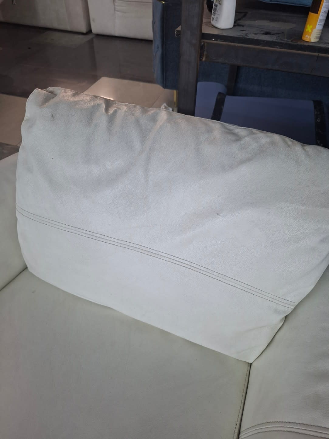 Close-up of back cushion on used white leather single armchair showing deflation and wear