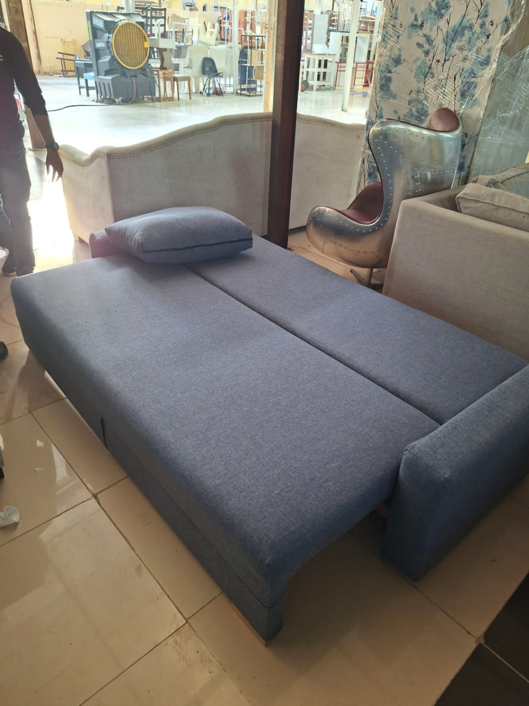 New 3-seater grey sofa bed fully flat from alternate angle showing fabric and wooden legs at Bufaisal Ajman