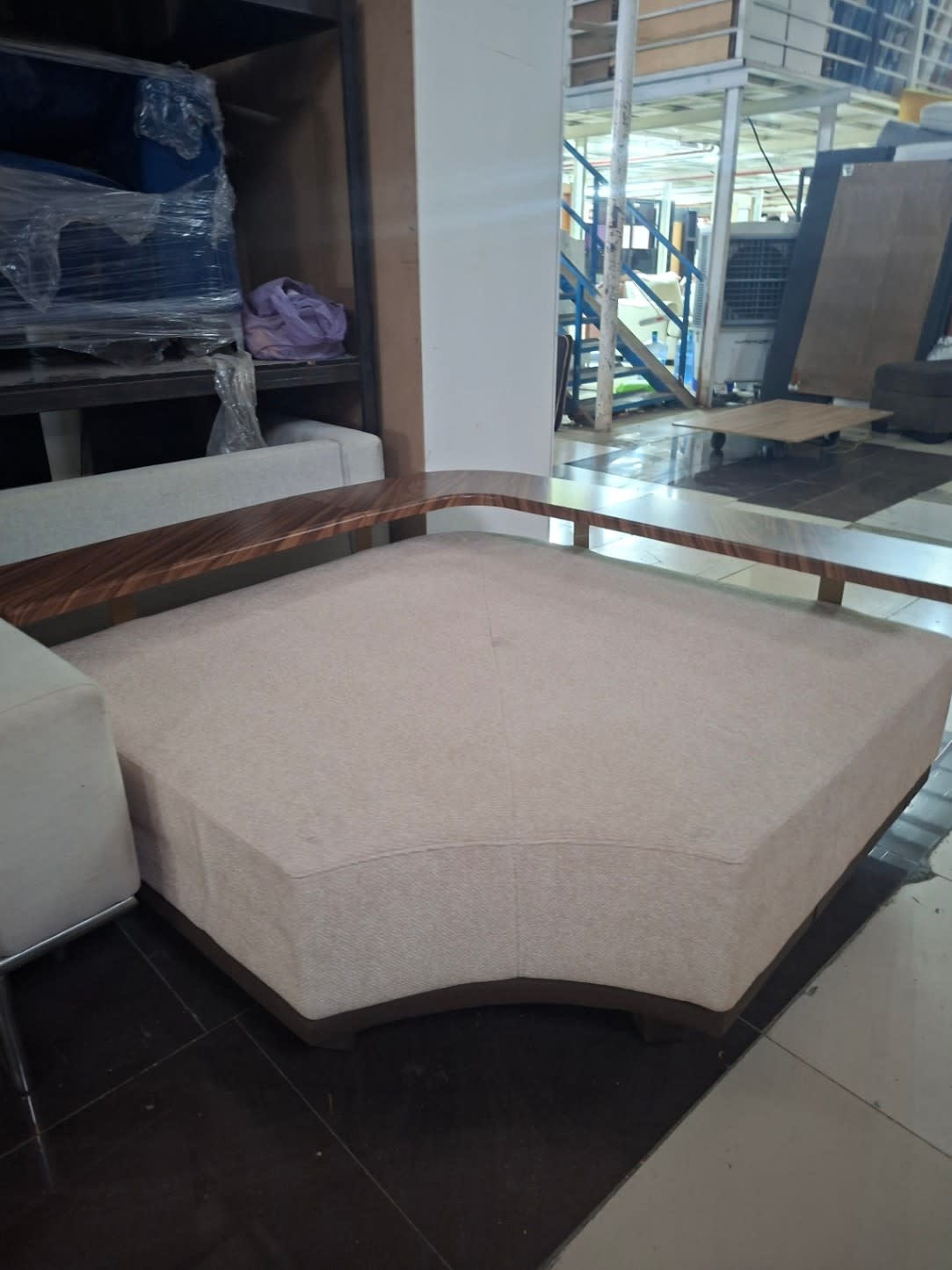 Corner detail of used beige corner ottoman showing curved walnut wood base and fabric upholstery