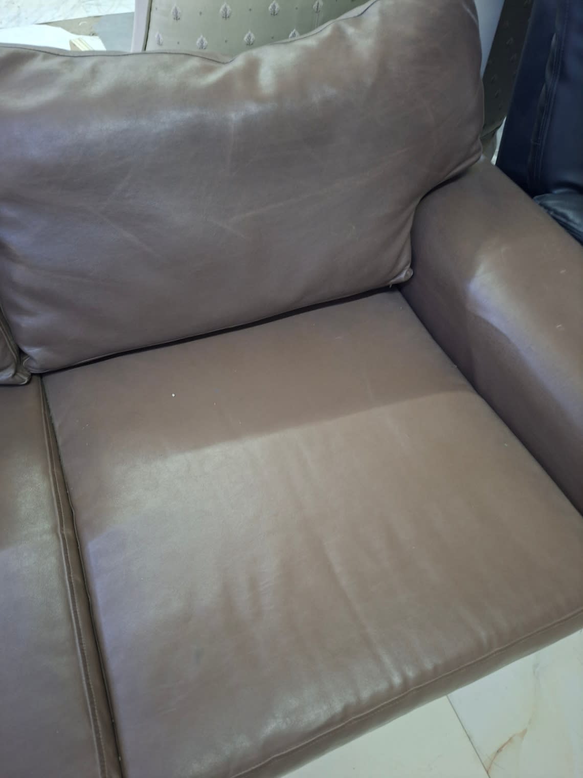 Detail shot of used 3-seater brown leather sofa seat cushion showing creasing and fading at Bufaisal Ajman