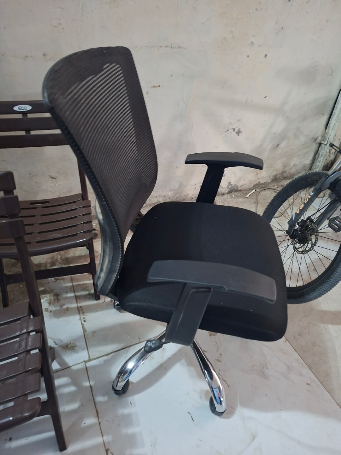 Side profile of used black mesh office chair showing T-bar armrest and chrome caster base