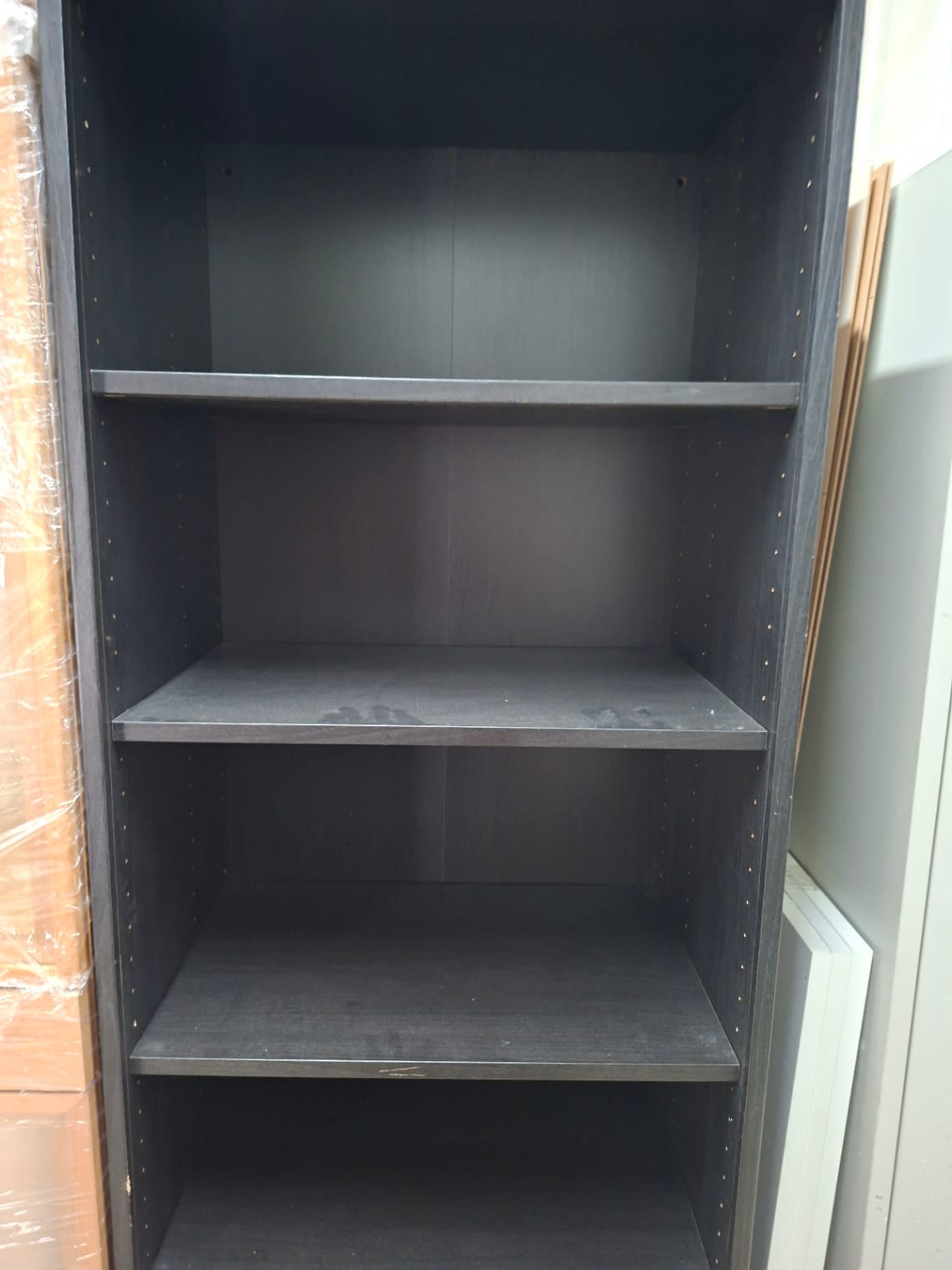 Close-up of lower shelves on used dark brown open shelving unit showing minor scuff marks and dust