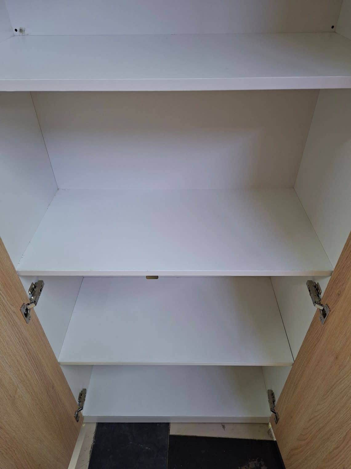 Close-up of interior shelves of used 2-door storage cupboard showing clean white finish