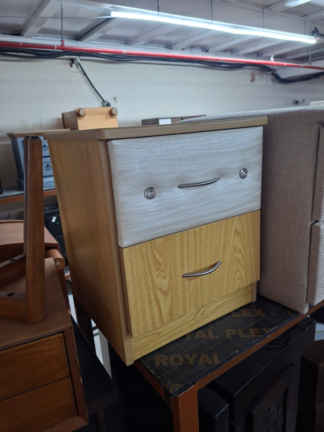 Angled view of used 2-drawer bedside table showing two-tone oak and white laminate finish at Bufaisal Ajman