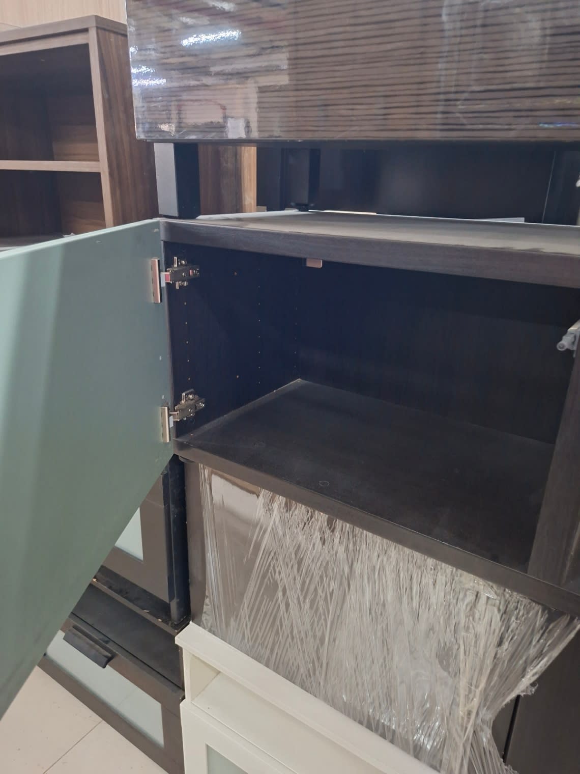 Interior detail of lower sage green glass door cabinet on used black TV stand at Bufaisal Ajman