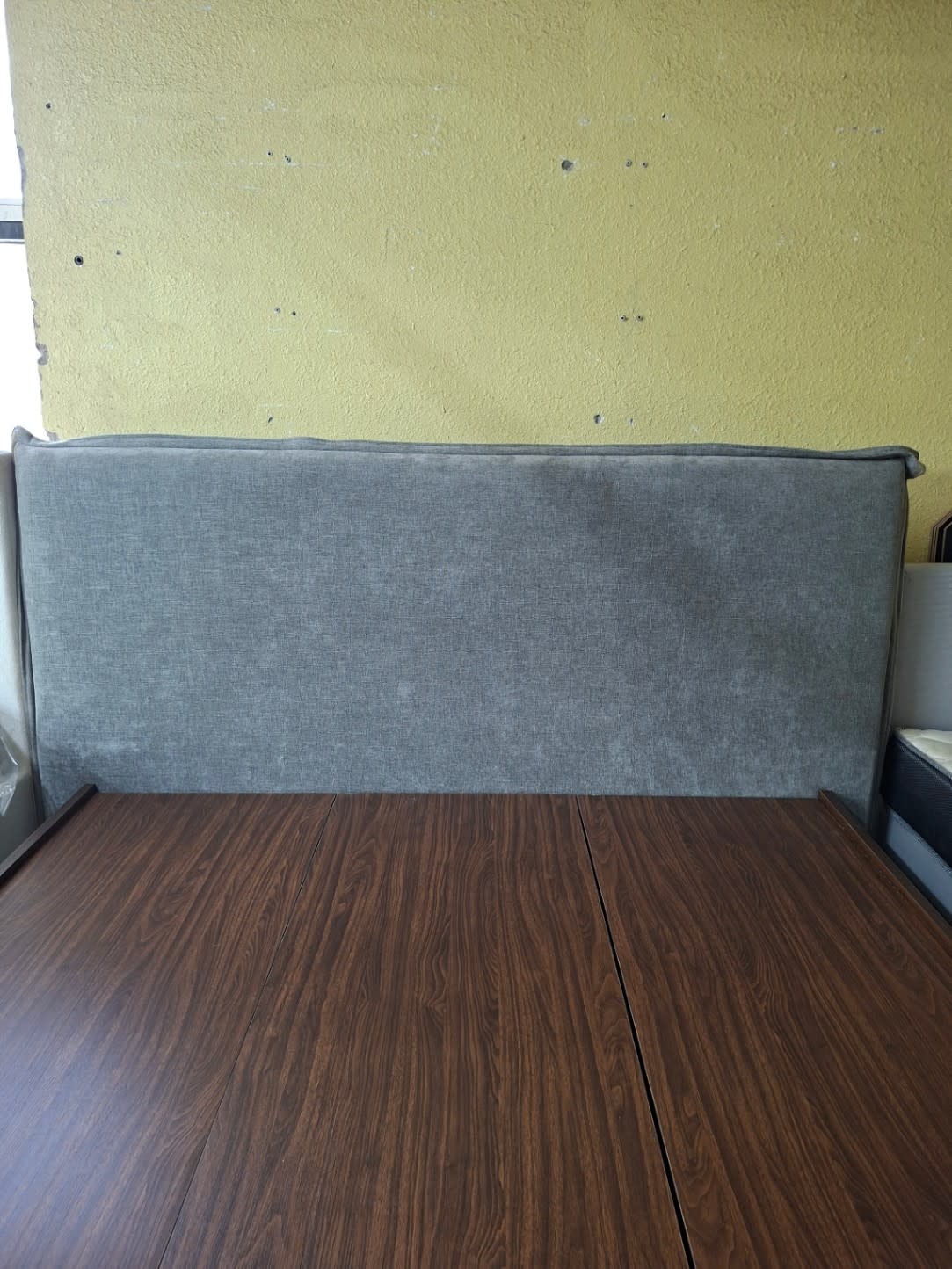 Close-up of grey upholstered headboard on used king bed frame showing fabric texture and condition