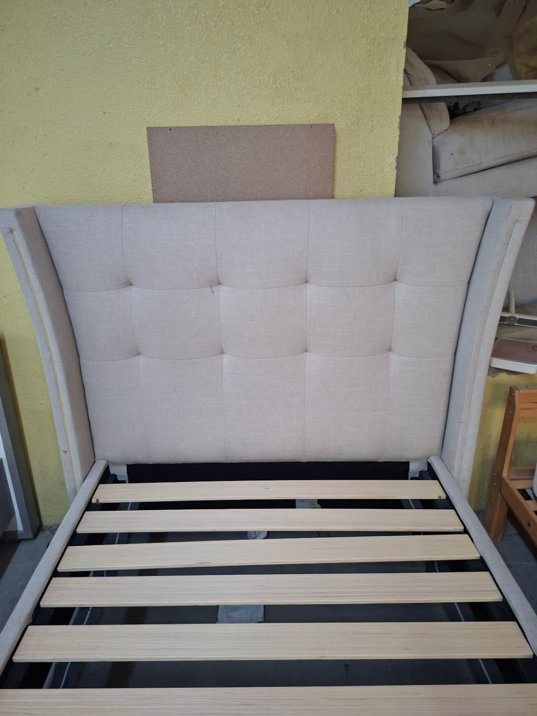 Close-up of tufted headboard on used beige wingback bed frame showing fabric condition