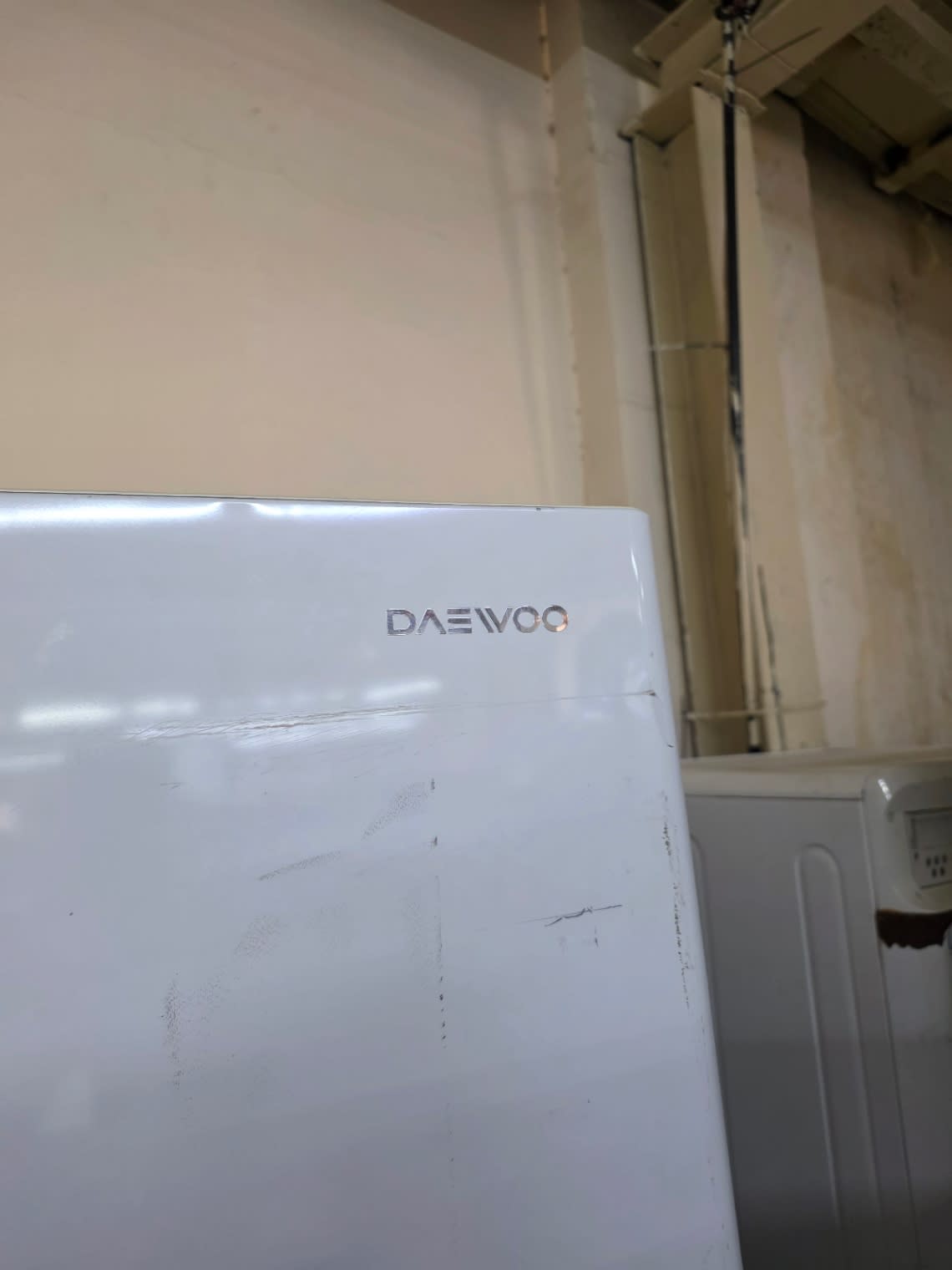 DAEWOO logo and upper door panel of used white refrigerator with visible surface scratching