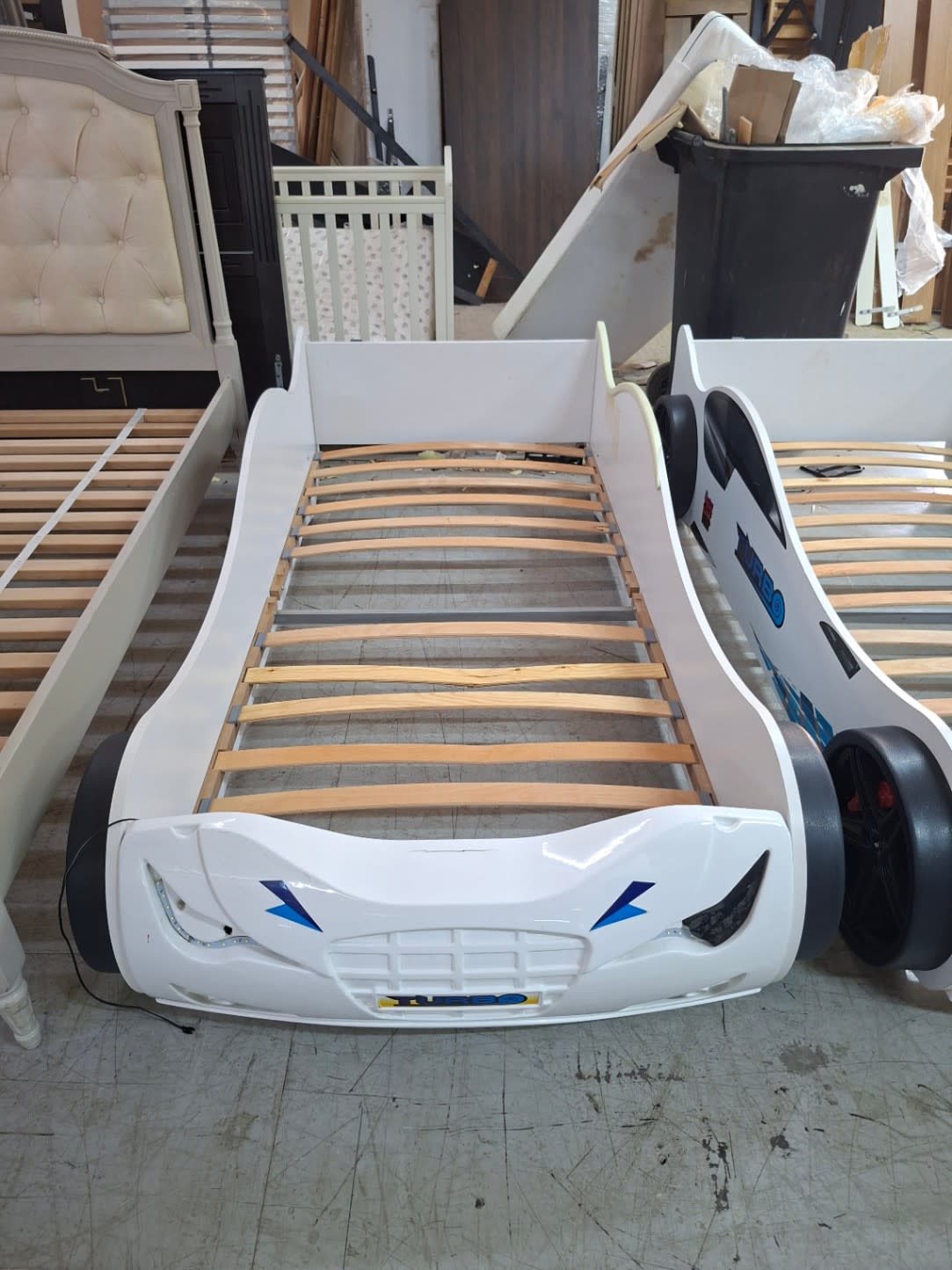 Front angle of used white race car kids bed frame showing minor scuffs and loose LED wire at Bufaisal Ajman