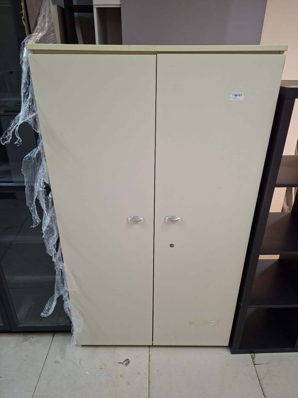 Front view of used two-door cream storage cupboard showing Bufaisal barcode label on right door