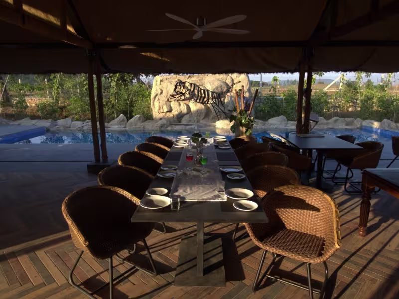 Poolside dinner table setup at LeMoor restaurant, with rattan chairs, a long set table, the carved tiger rock sculpture in the background and the resort pool visible to one side.