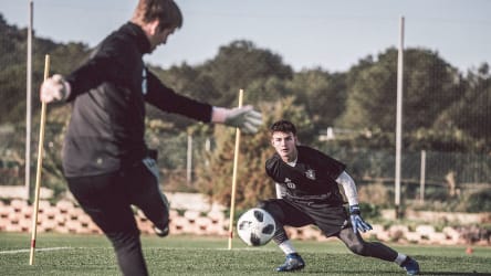 Die Torhüter schießen sich gegenseitg ein. © Philipp Reinhard 2018 Ein Torwart schießt den Ball in Richtung eines anderen Torwarts, welcher in die Richtung springt, in die der Ball geschossen wurde. Im Hintergrund sieht man Stangen, die so platziert sind, dass sie ein Tor darstellen. © Philipp Reinhard 2018