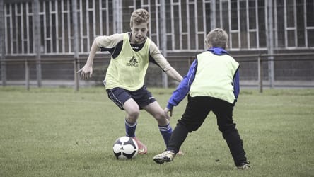 Im 1 vs. 1 sollen kreative Ansätze probiert werden, um sich durchzusetzen © 2019 Philippka-Sportverlag Ein Junge dribbelt mit den Ball mit dem rechten Außenriss um an seinem Gegenspieler, der ihm frontal gegenüber steht, vorbei zu kommen. © 2019 Philippka-Sportverlag