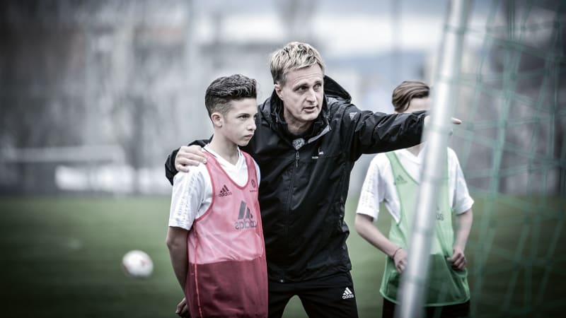 Durch ständigen Dialog fühlen sich die Spieler wohler im Training und können das volle Potenzial abrufen © 2019 Philippka-Sportverlag Ein Trainer widmet sich einem Spieler besonders. Er fasst ihm an die Schulte und deutet mit dem Finger auf etwas außerhalb des Bildes und erklärt etwas. Ein Zweiterjunge steht daneben und hört zu. © 2019 Philippka-Sportverlag