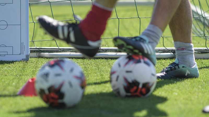 Ein Taktikboard steht beim DFB Elite Youth Coach Development Workshop neben einem Tor. Im Vordergrund sind Fußbälle und Beine von Teilnehmern des Workshops zu sehen.