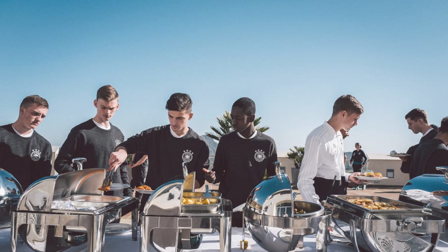 Spieler einer deutschen U-Mannschaft bedienen sich an einem Buffet.