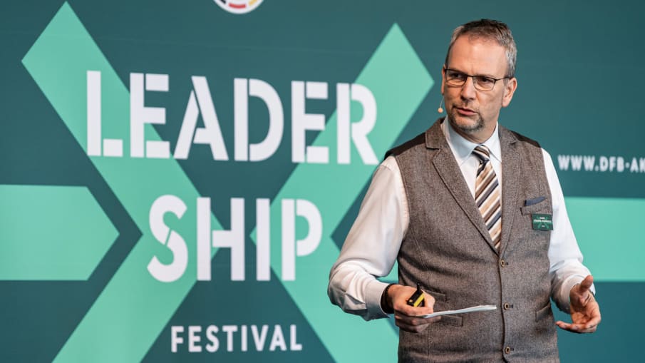 Mark Hübner-Weinhold hält einen Vortrag auf dem Leadership Festival 2019 © 2019 Philipp Reinhard Mark Hübner-Weinholf hat Karteikarten in der Hand und hält vor einer grünen Wand mit der Aufschrift "Leadership Festival" einen Vortrag.