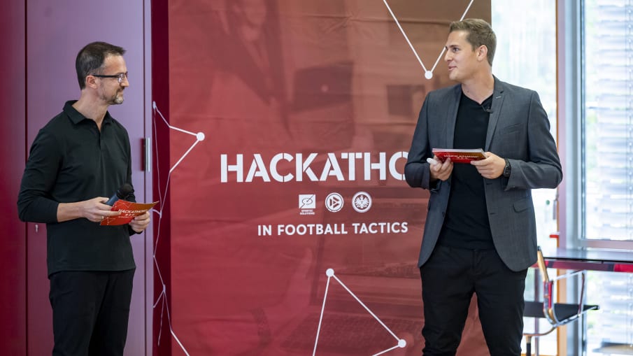 Fredi Bobic und Pascal Bauer unterhalten sich während der Eröffnungsrede © 2020 Getty Images Fredi Bobic steht neben Pascal Bauer vor einem Hackathon² Banner und redet während seiner Rede mit ihm. © 2020 Getty Images