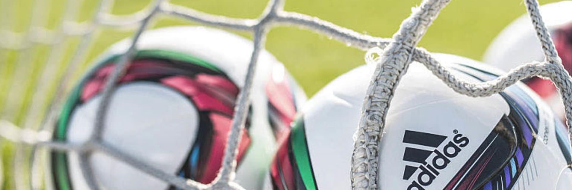 Auf einem Fußballfeld liegen drei Fußbälle in einem Tornetz.