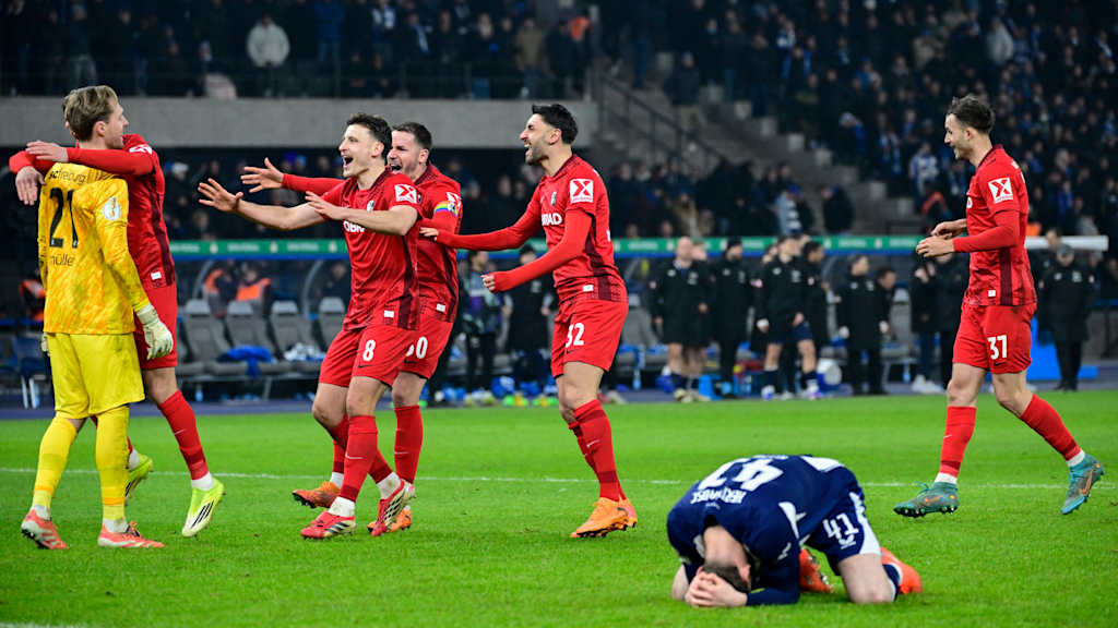 Freiburg players in red kits rush to celebrate with their goalkeeper.