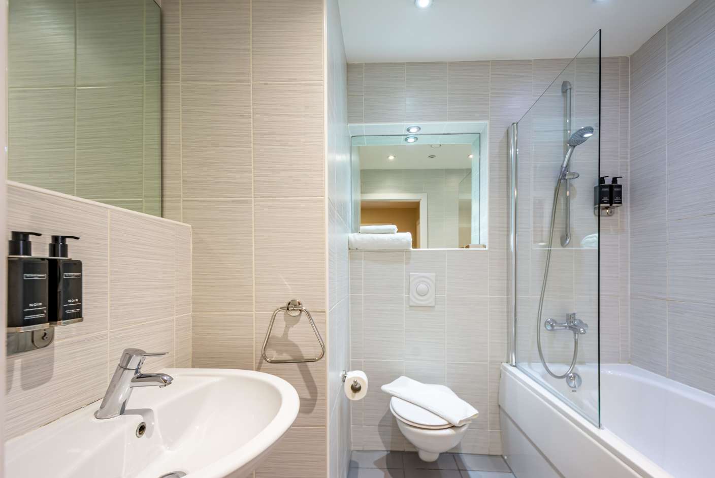 Apartment bathroom with bathtub, shower over bath, sink, toilet and The White Company toiletries.