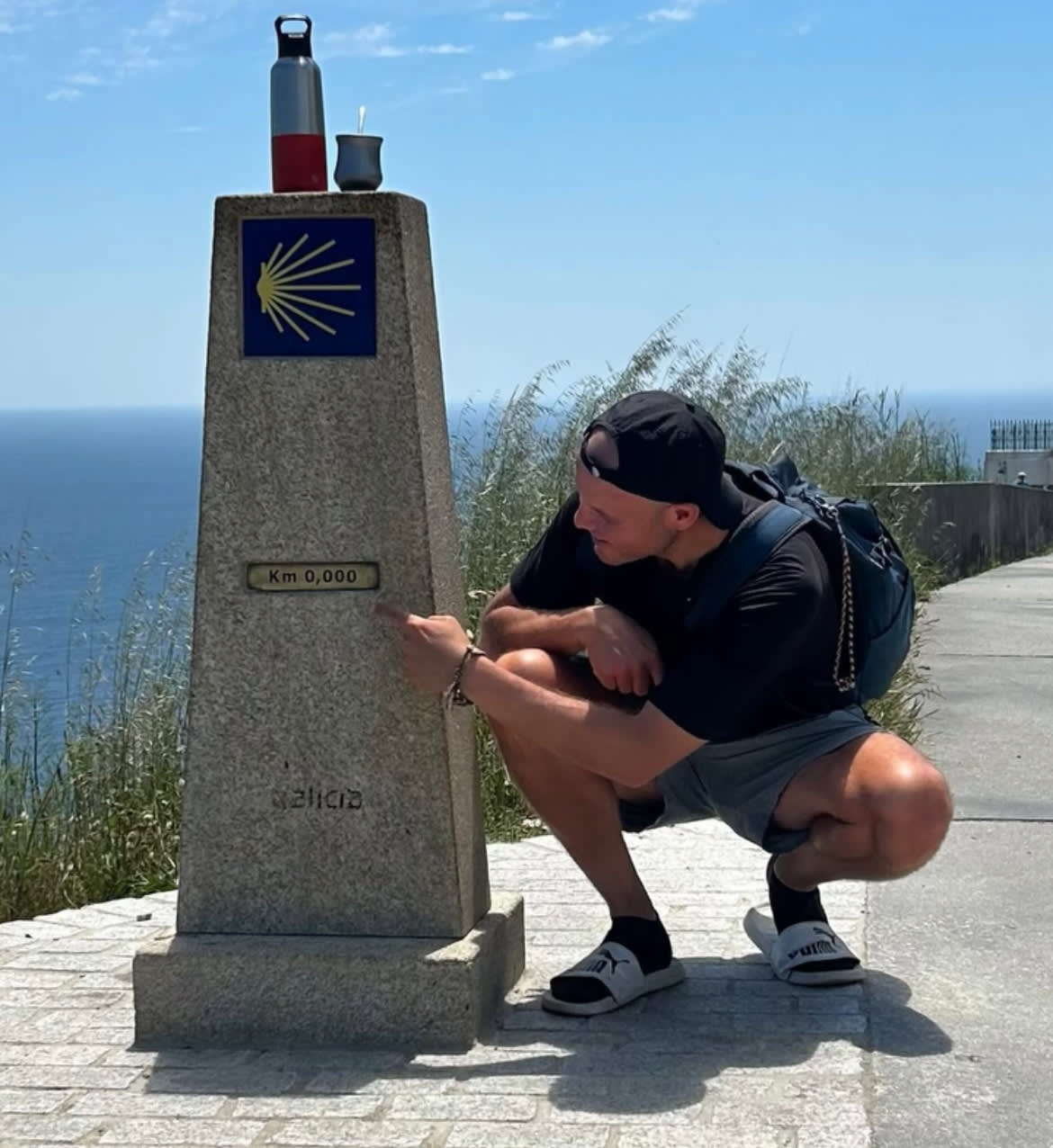 Persona en el Cabo de Finisterre señalando el mojón del kilómetro cero
