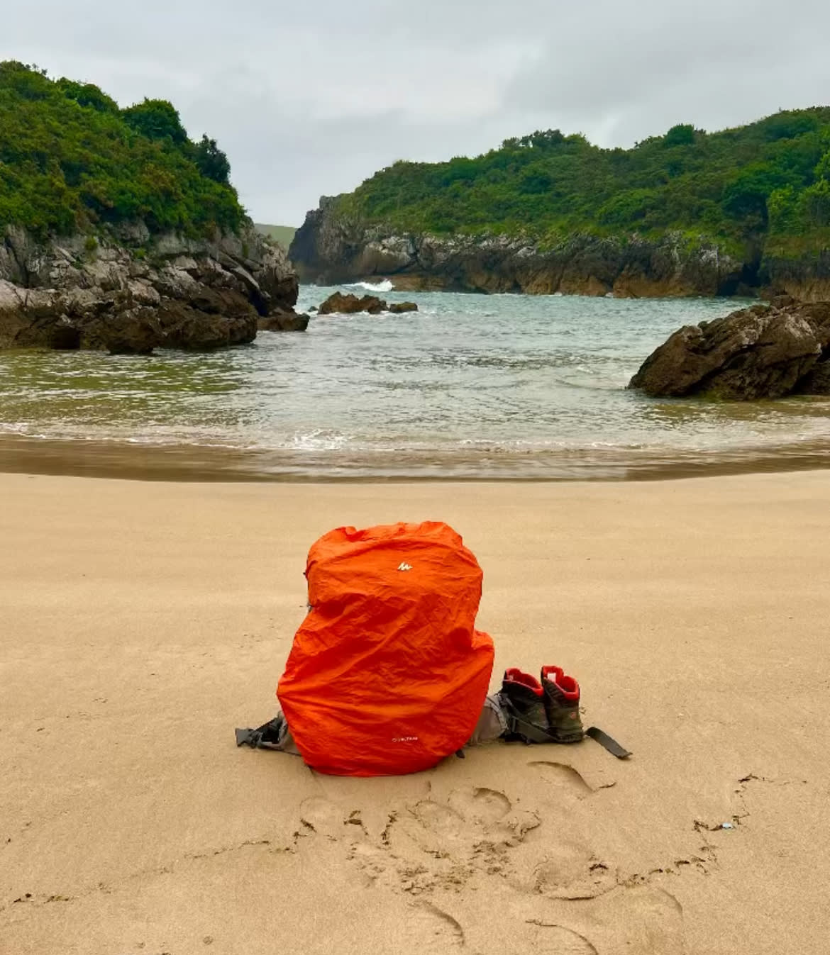 Mochila y botas de trekking frente a una playa en Asturias