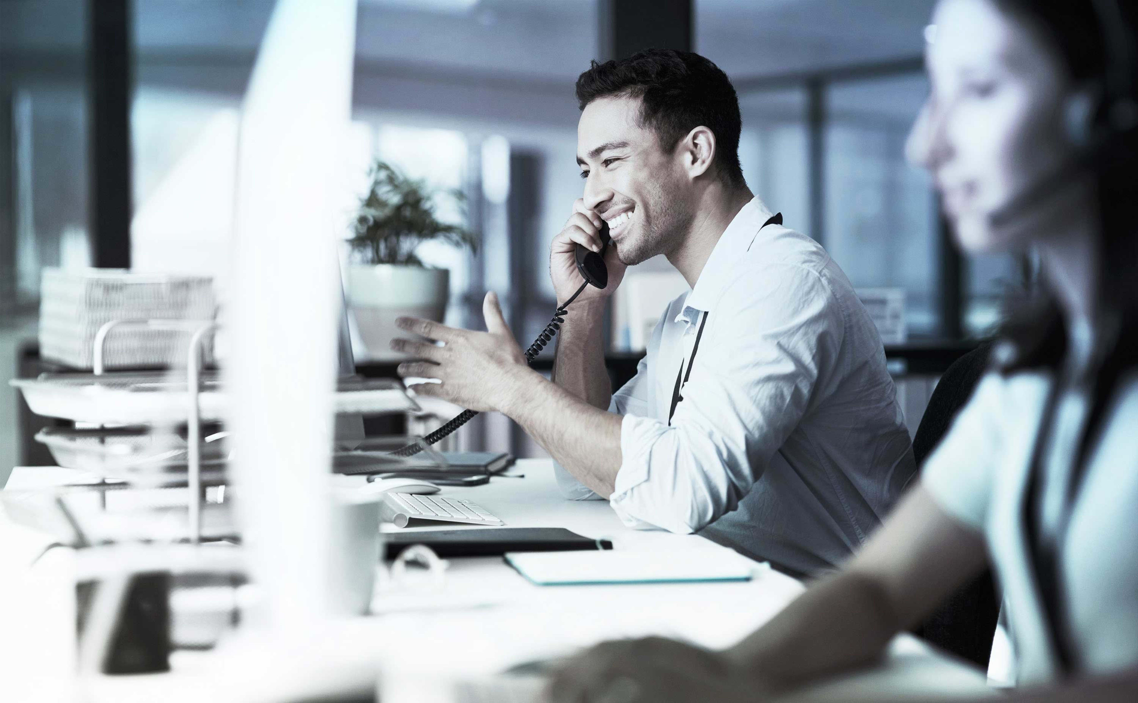Büro-Mitarbeiter am Telefon, im Vordergrund eine Kollegin.