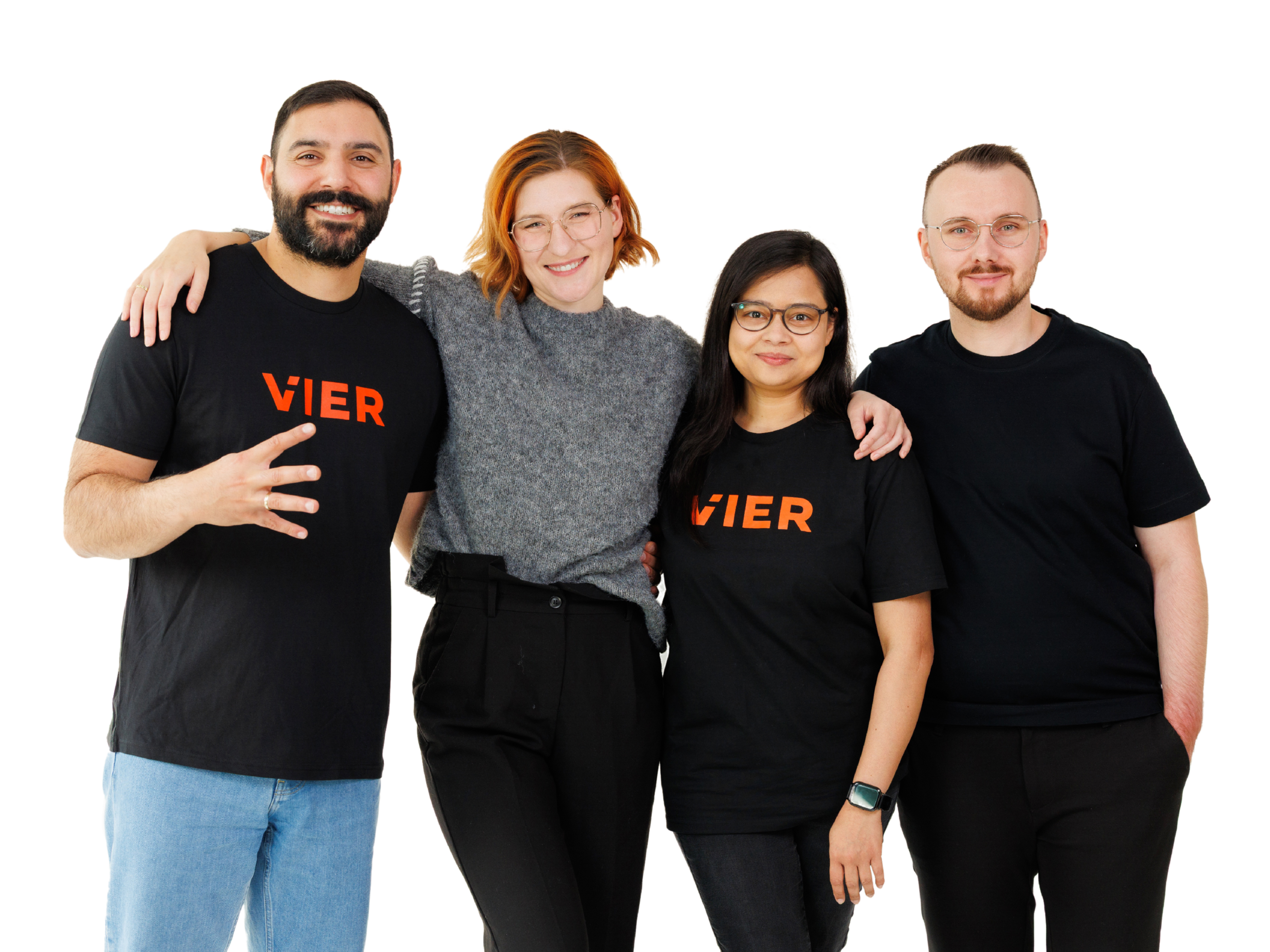 Vier lächelnde Personen – zwei Männer und zwei Frauen – stehen gemeinsam im Vordergrund vor einem schlichten weißen Hintergrund; alle tragen schwarze T-Shirts mit einem orangefarbenen „VIER“-Logo.