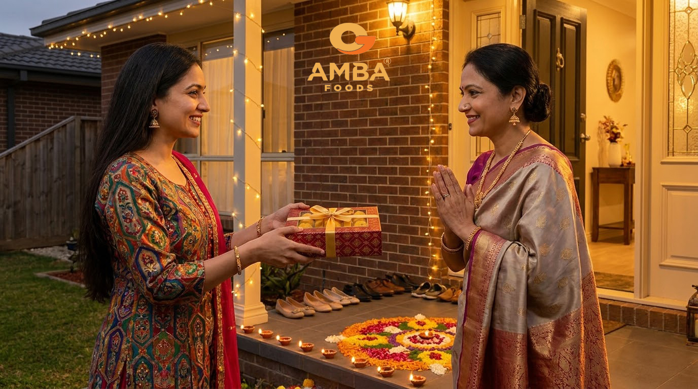 Guest handing a box of Indian sweets to a smiling host at the door of a home decorated for Diwali