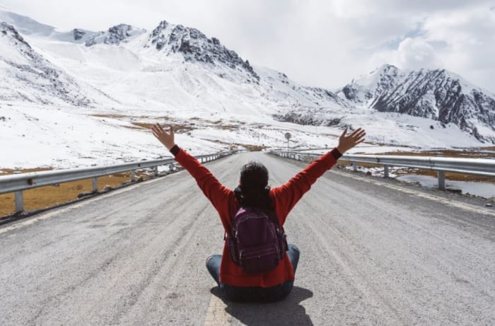 woman-seating-in-middle-of-a-road-in-mountains-with-her-arms-in-the-air.jpeg