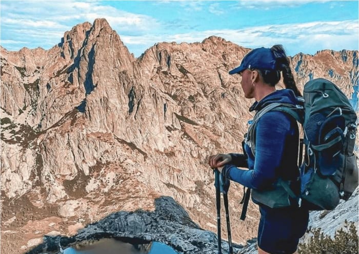 reiseaccessoires-frau-mit-kappe-rucksack-und-wanderstoecken-blickt-auf-ein-bergmassiv.JPG
