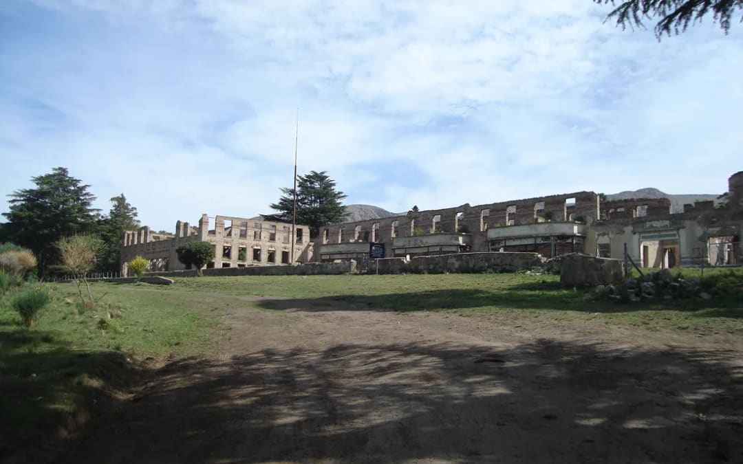 Las ruinas del Club Hotel de la Ventana vistas casi desde el mismo lugar que la postal: el edificio largo sin techo, con los vanos de las ventanas vacíos y la sierra detrás.