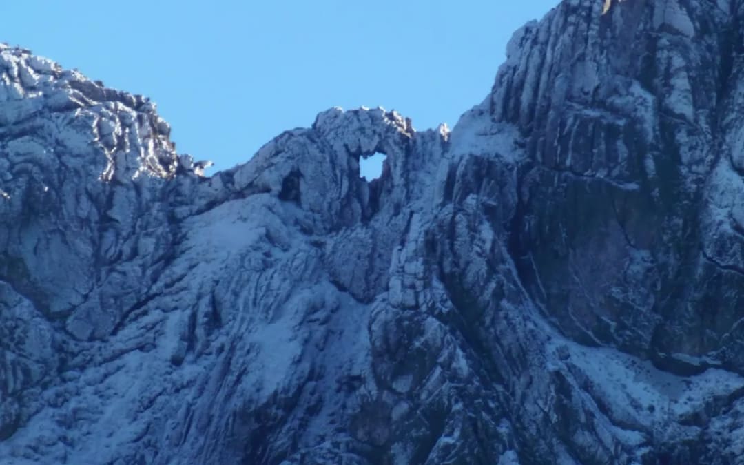 Primer plano del cerro Ventana con nieve: se ve el hueco en la roca que le da el nombre a la sierra, y las capas de piedra inclinadas por el plegamiento.